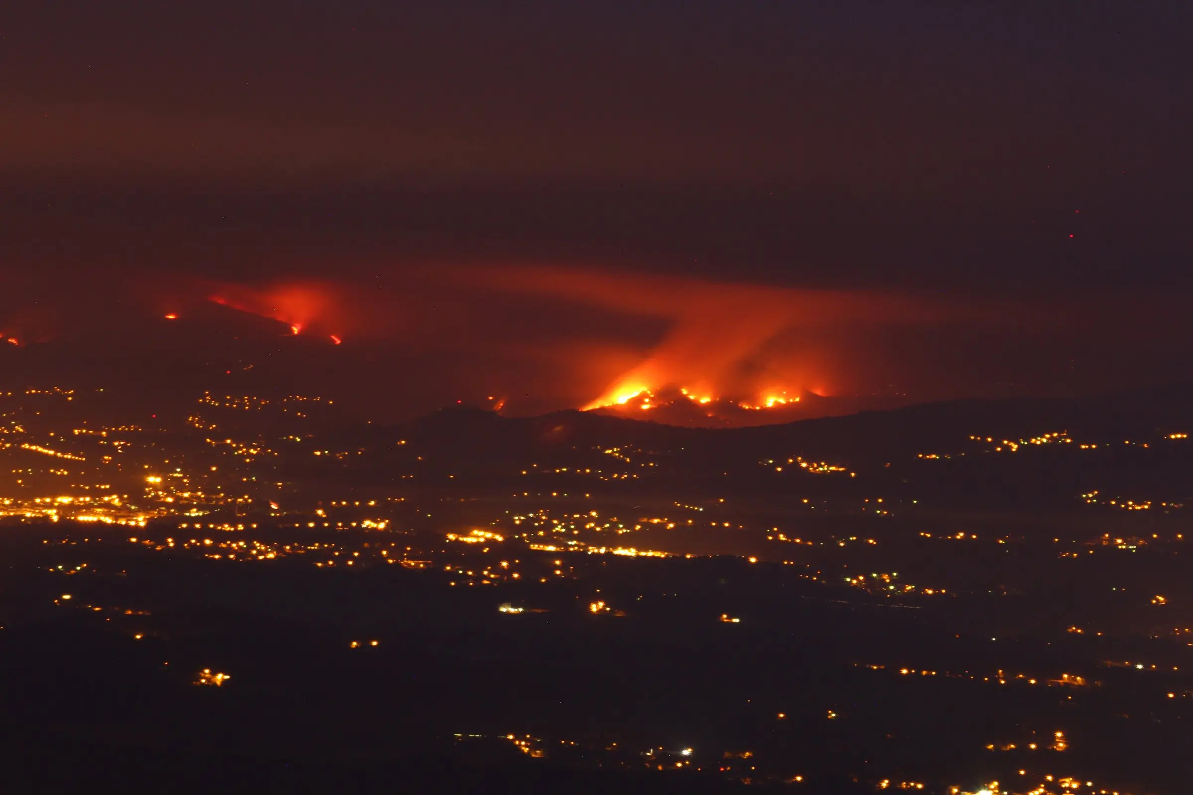 Incendio forestal de noche en una sierra, con las luces de los pueblos en primer plano